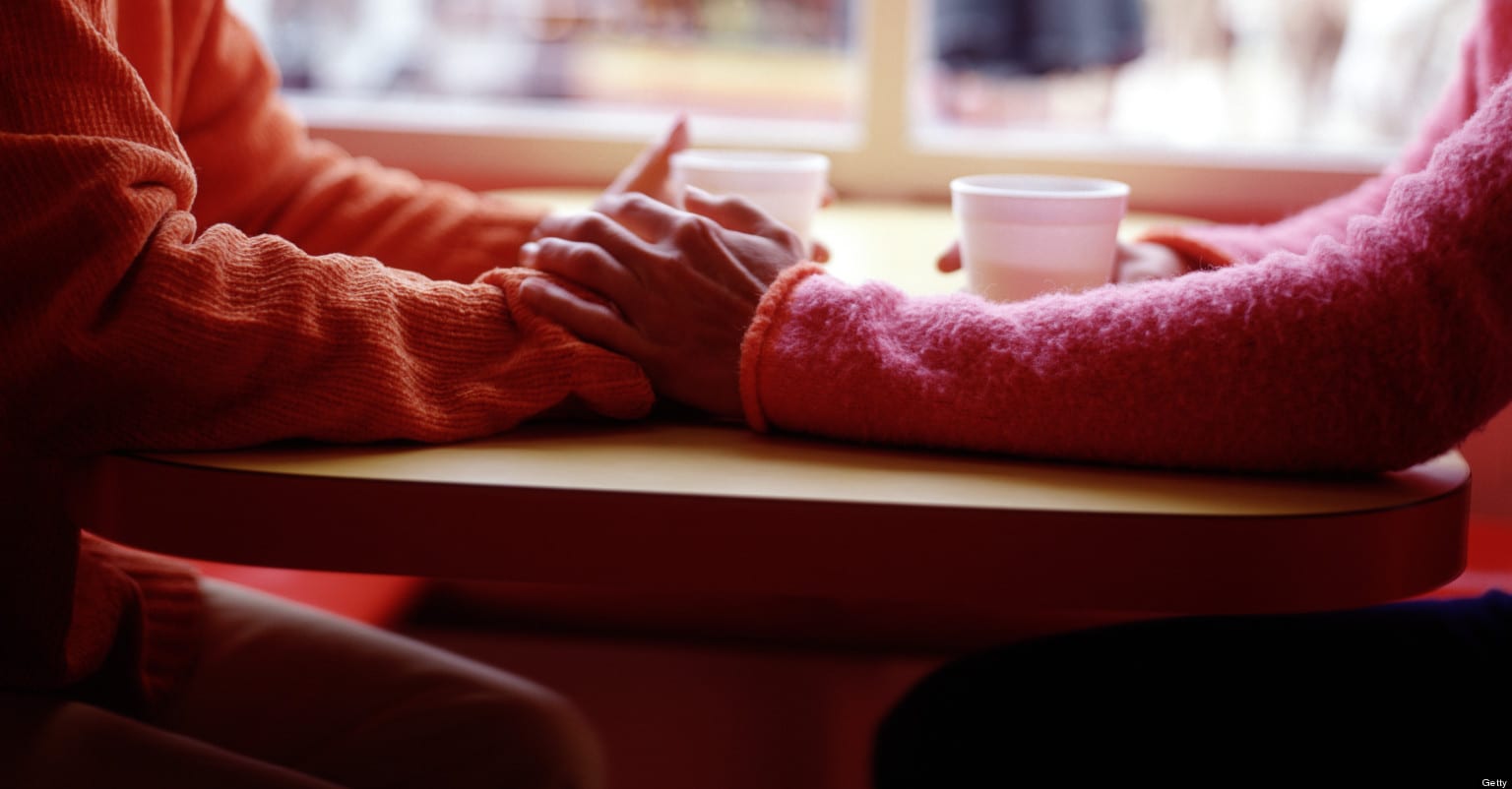 Two women at cafe table holding hands