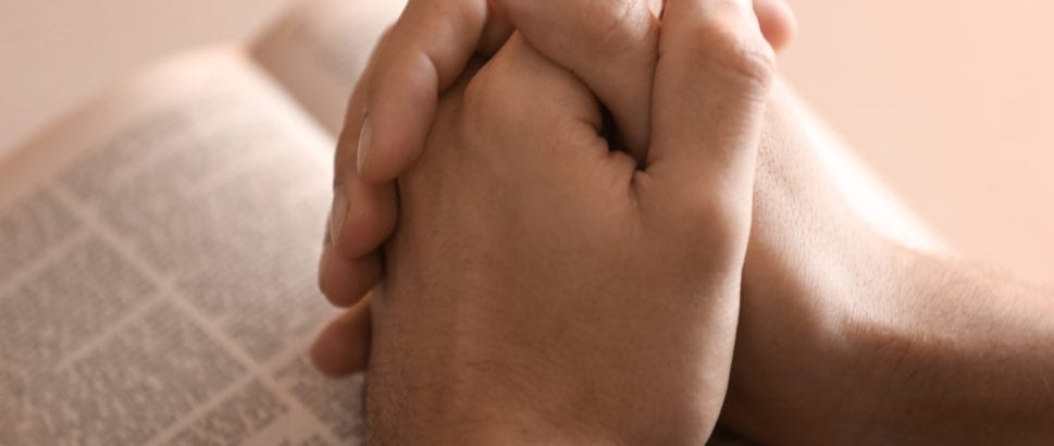 Male hands folded in prayer over open Bible, closeup